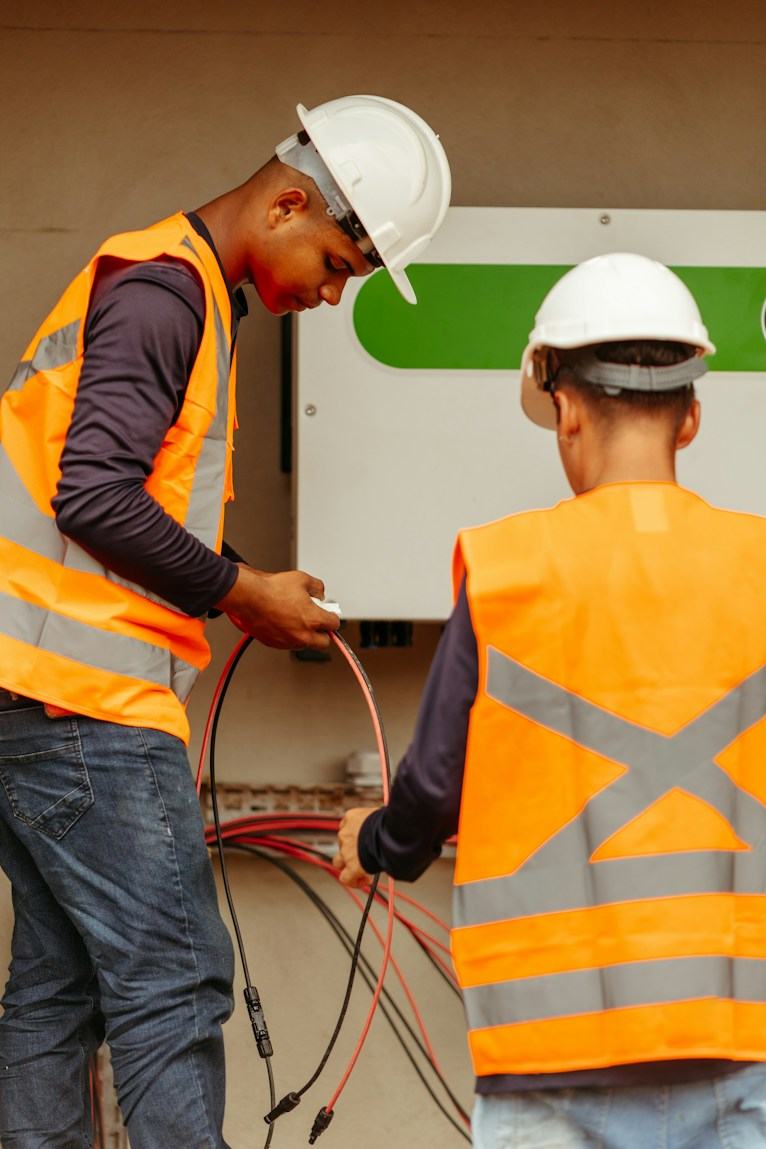 Two workers in hard hats and orange vests handling electrical cables